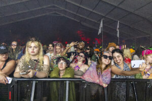 Crowd of festival-goers behind a barrier at night, many smiling and posing for photos.
