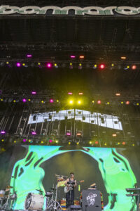 Concert stage with bright multicolored lights, large video screen, and a band performing on stage.
