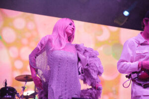 Female singer in a shiny silver sequin dress holding a fluffy feather boa under pink stage lights on a performance stage.