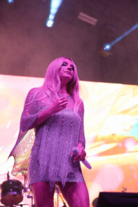 Female singer on stage, pink lighting, holding a microphone and wearing a shimmering purple dress.