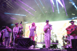 Live band on stage performing with bright purple and blue lights, singer in a sparkly dress center stage