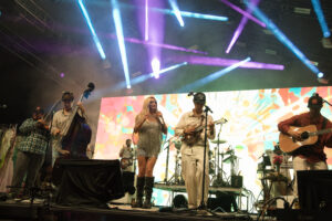 Live band on stage performing with bright blue and purple laser lights and a colorful backdrop behind them.