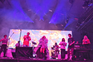 Live concert stage with performers under purple lights and a fiery digital backdrop.