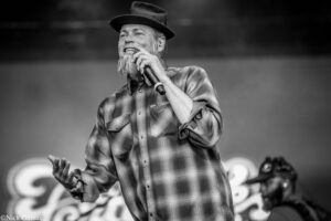 Male singer with a beard and hat performing on stage, holding a microphone.