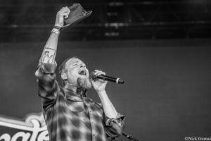 Male singer on stage raising a hat while singing into a microphone, in black and white