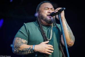 Male vocalist with dreadlocks and tattoos singing into a microphone on stage.