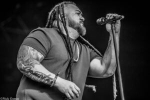 Male singer with long dreadlocks and tattoos holding a microphone on stage.
