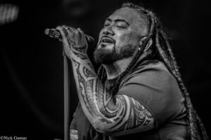 Male singer with dreadlocks and full sleeve tattoos singing passionately into a microphone on stage. (informative)
