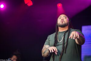 Male rapper on stage under purple lights, reaching toward the crowd.