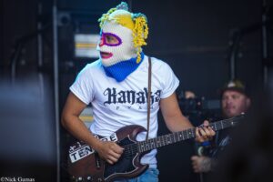 Musician wearing a colorful knitted mask and playing an electric guitar on stage.