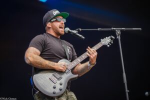Male guitarist performing on stage, singing into a microphone while playing a silver electric guitar.