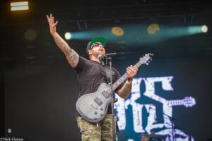 Guitarist on stage raises his left hand while playing a gray electric guitar.