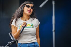 Singer on stage wearing sunglasses and a white T-shirt, gripping a microphone while performing.