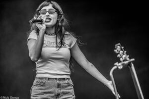 Female singer wearing sunglasses, holding a microphone and singing on stage (black and white).