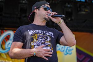 Male singer performing on stage, wearing a cap and sunglasses, holding a microphone close to his mouth.