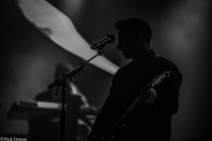 Silhouette of a guitarist performing on stage, with a microphone on a stand in front, dim lighting behind.