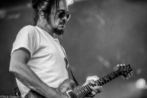 Musician wearing sunglasses, playing an electric guitar on stage in black-and-white.