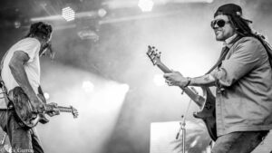 Two electric guitarists performing on a smoky stage during a live concert (black and white).
