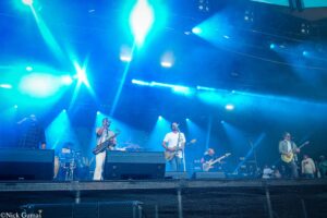 Band performing on a blue-lit stage with musicians playing guitars and a saxophonist