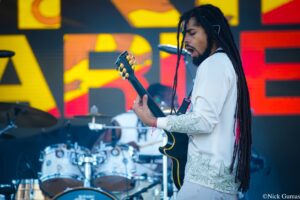 Guitarist with long dreadlocks playing an electric guitar on stage during a performance.