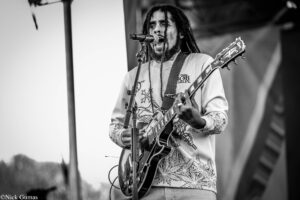 Black-and-white photo of a male guitarist singing into a microphone while playing an electric guitar on stage