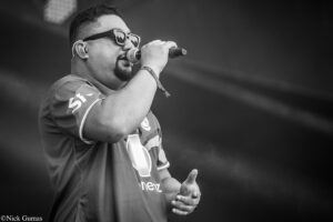 Male singer wearing sunglasses and in-ear monitor performs into a microphone on stage (black-and-white photo).