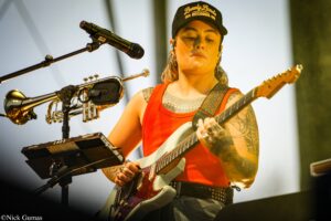 Musician wearing a black cap with Lonely Lands Records logo, playing an electric guitar on stage.