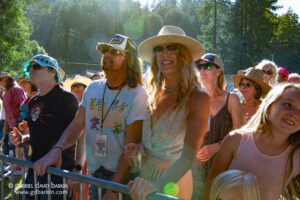 Crowd at an outdoor event behind a metal barrier, people wearing hats and sunglasses in sunlight.