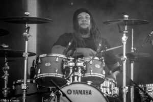 Drummer wearing a beanie playing a Yamaha drum kit on stage (black-and-white photo).