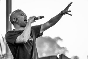Black-and-white photo of a male singer on stage, microphone in hand, left arm raised upward in a dynamic performance pose.