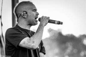 Male singer performing into a handheld microphone on stage, wearing a dark shirt (black-and-white photo).