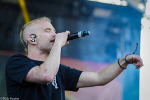 Male singer performs on stage, gripping a wireless microphone with an in-ear monitor visible in his ear.