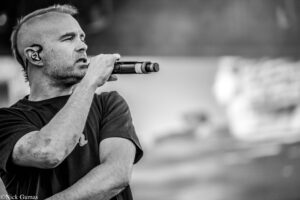 Male singer on stage, gripping a handheld microphone and singing into it, wearing an in-ear monitor in his left ear (black-and-white photo).