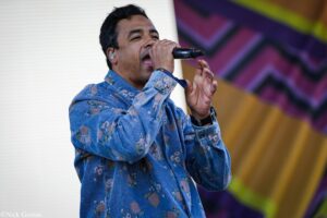 Male singer wearing a floral blue denim jacket performs into a handheld microphone on stage.