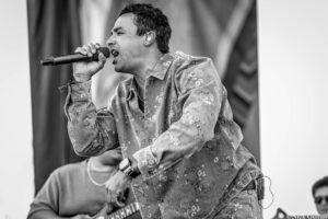 Male singer wearing a floral denim shirt, passionately singing into a handheld microphone on stage (black-and-white photo).