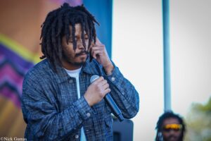 Male singer with dreadlocks, eyes closed, singing into a handheld microphone on stage.
