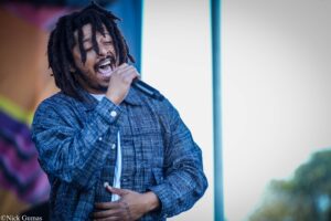 Male singer with dreadlocks passionately performing on stage, microphone in hand, eyes closed.