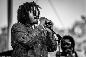 Male singer with dreadlocks holding a microphone on stage, performing passionately (black and white).