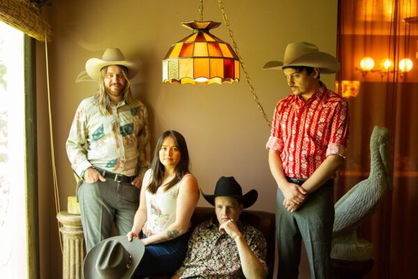 Four people in cowboy hats pose in a retro room with a Tiffany-style hanging lamp on themain light fixture.