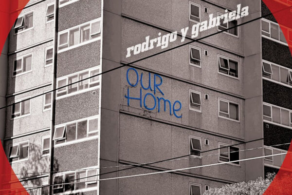 Album cover: grey apartment block with a red circular overlay and white text 'rodrigo y gabriela' plus blue 'OUR HOME'.