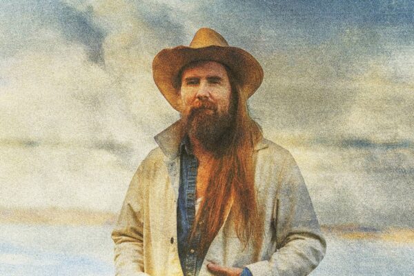 Album cover portrait of a bearded man in a wide-brim hat and beige jacket, standing outdoors.