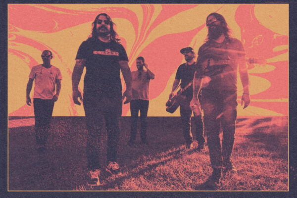 Five men in casual clothes stand on a grassy slope against a bold pink-orange, swirl-pattern backdrop.
